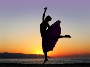 Dramatic image of a woman dancing by the ocean at sunset